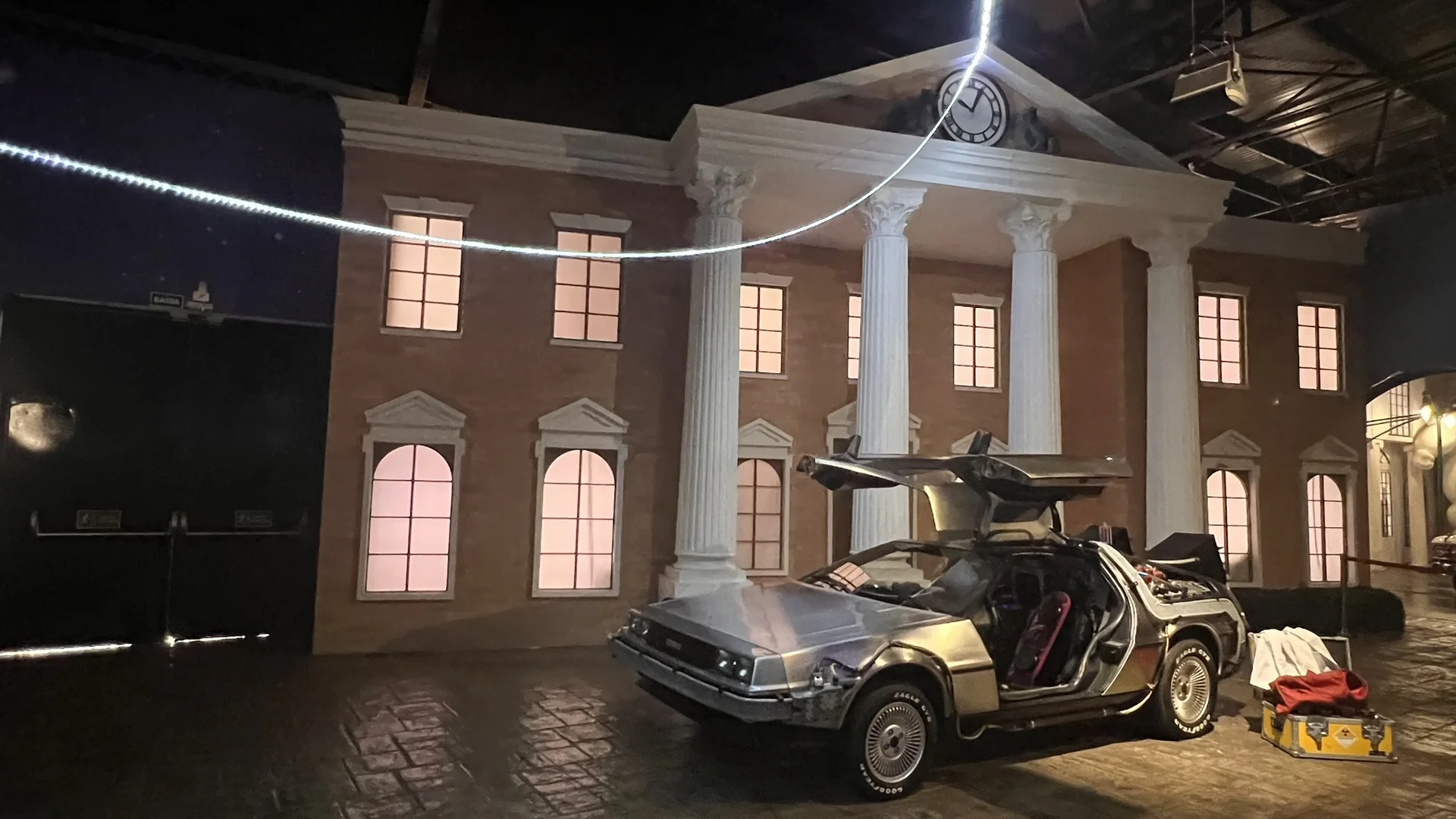 DeLorean de De Volta para o Futuro com as portas asa-de-gaivota abertas, em cenário reconstruído no Movie Cars